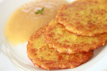 three vegan potato fritters on a white plate with apple puree on the side