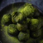 a stack of matcha energy balls on a black plate seen from above with a bite taken out of one of them