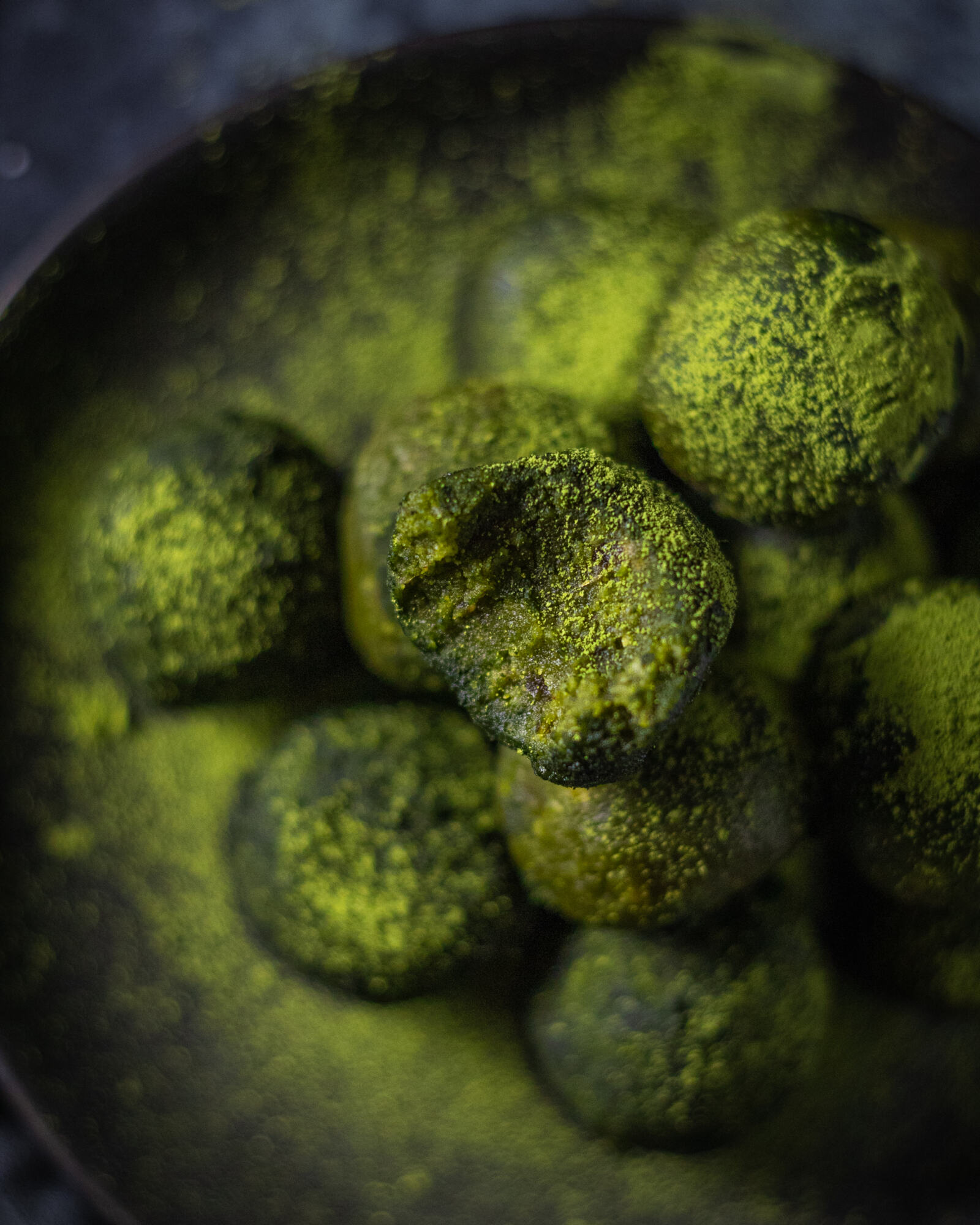 matcha energy balls on a black plate with an energy ball on the top that has a bite taken out of it