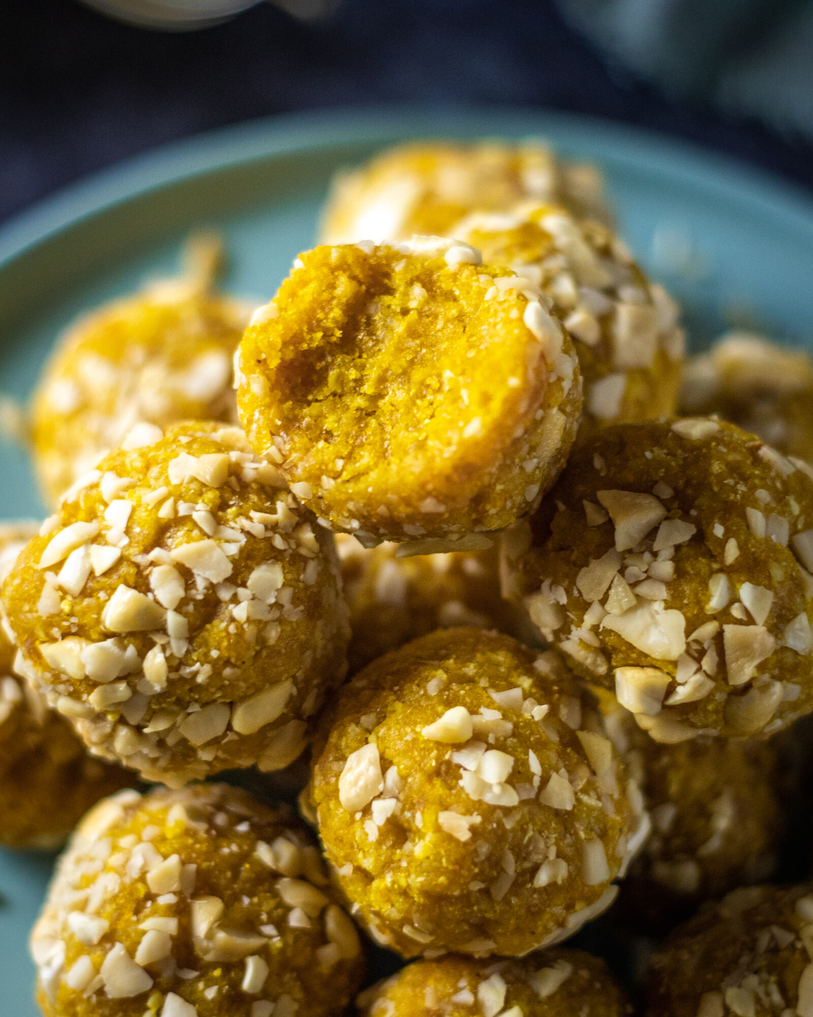 Vegan Turmeric Energy Balls stacked on a blue plate with a bite taken out of the one on the top