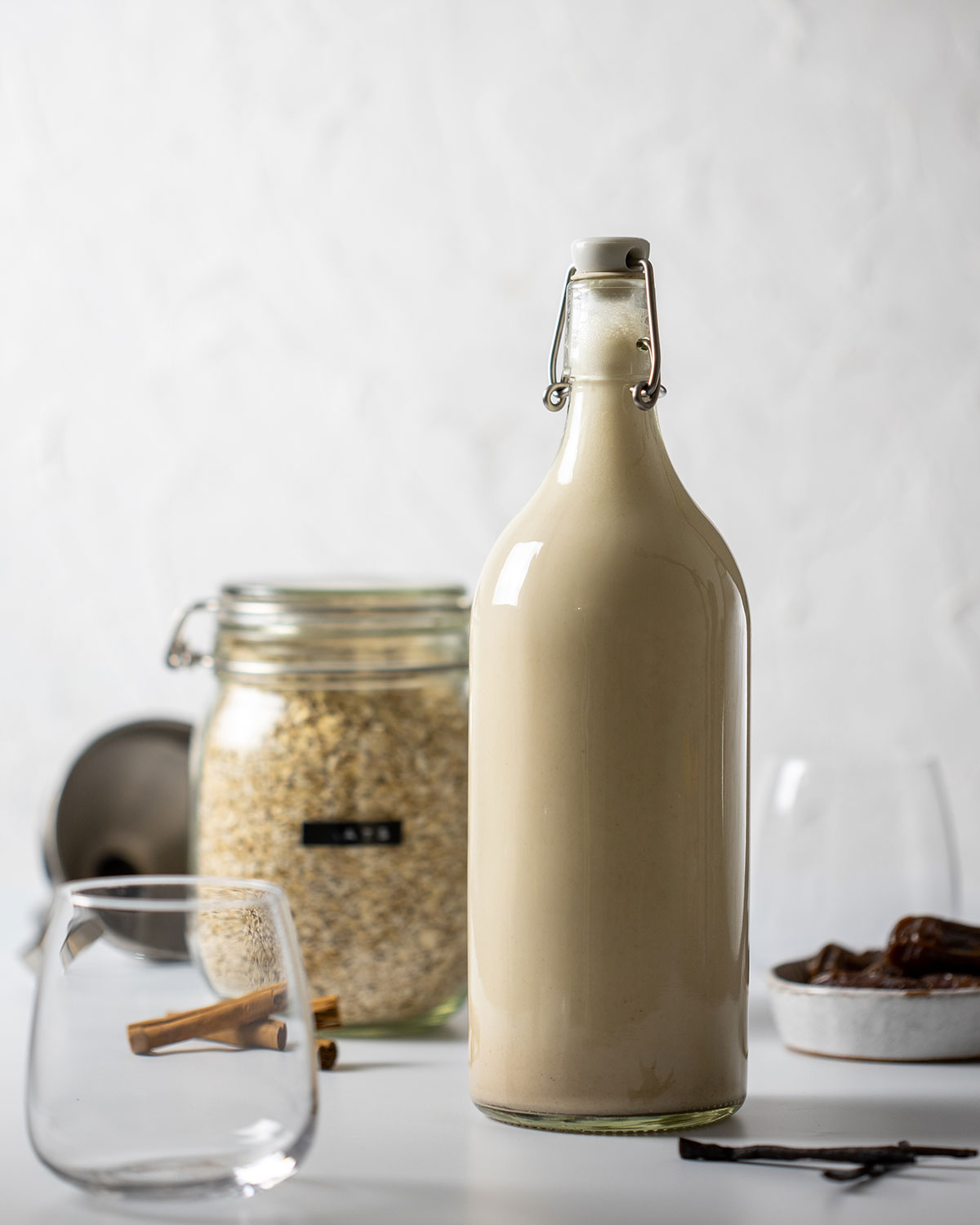 easy homemade oat milk in a tall glass bottle, filled to the top, surrounded by ingredients