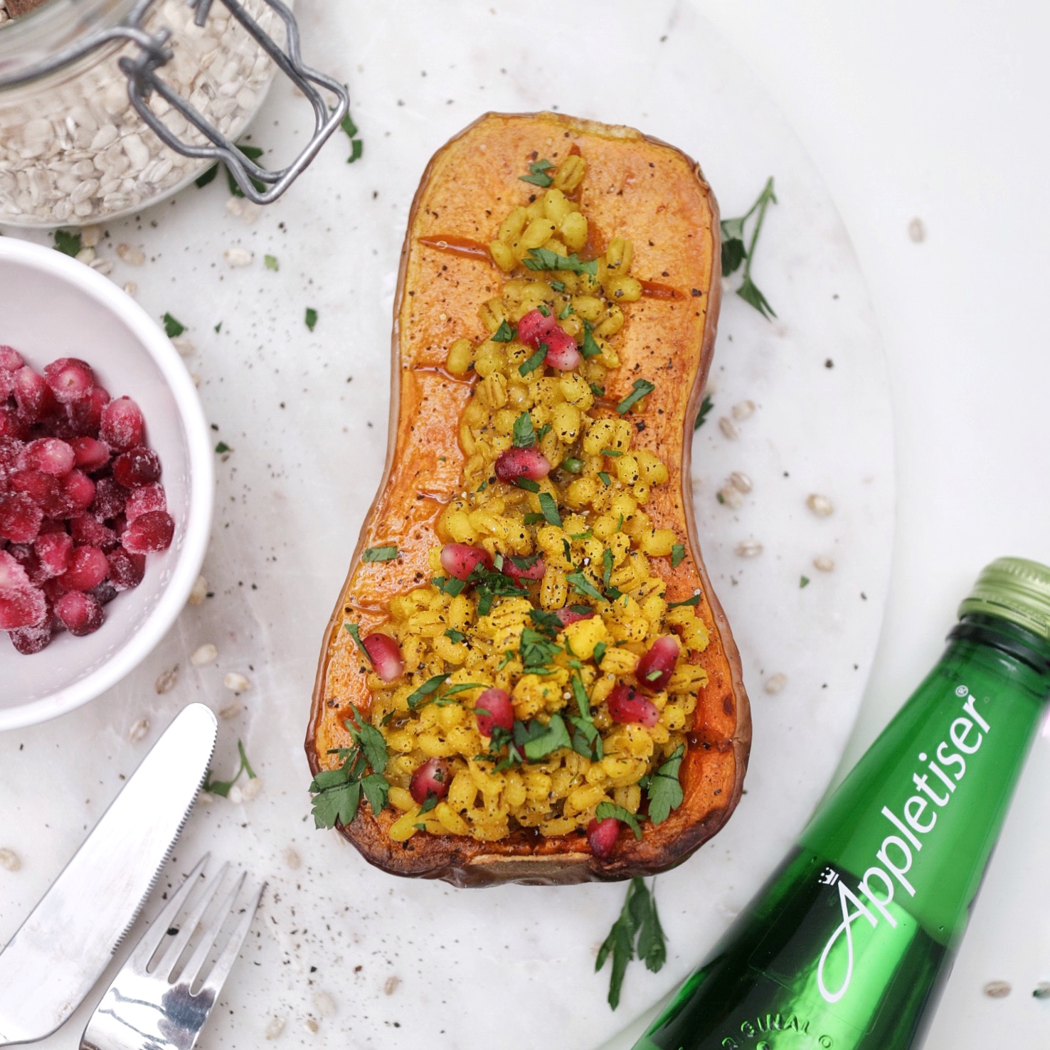 Half a stuffed butternut squash filled with curried barley and pomegranate seeds on top