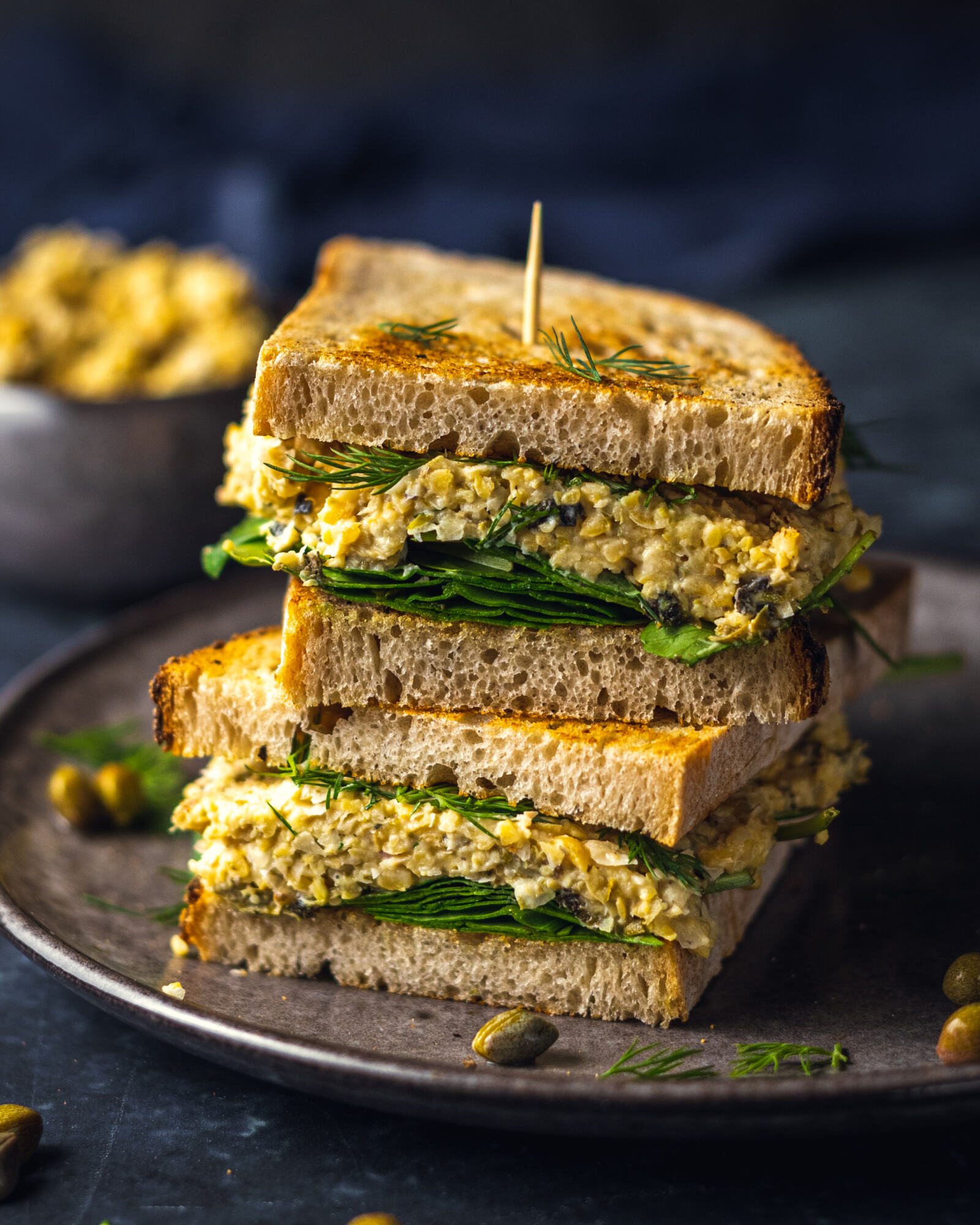 2 chickpea tuna sandwiches with added spinach on top of each other on a black plate