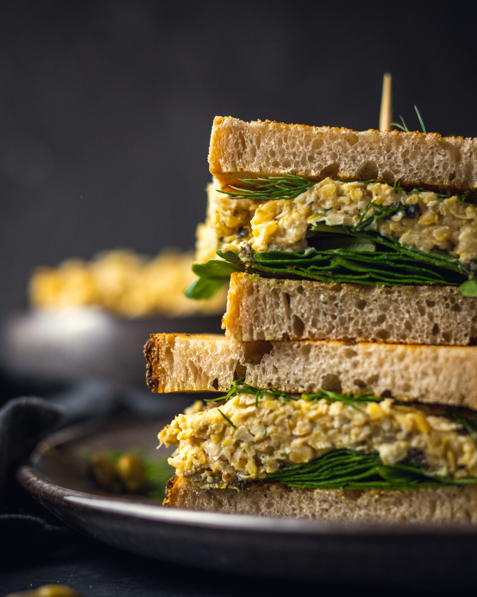 Two chickpea tuna sandwiches are placed on top of each other on a black plate.