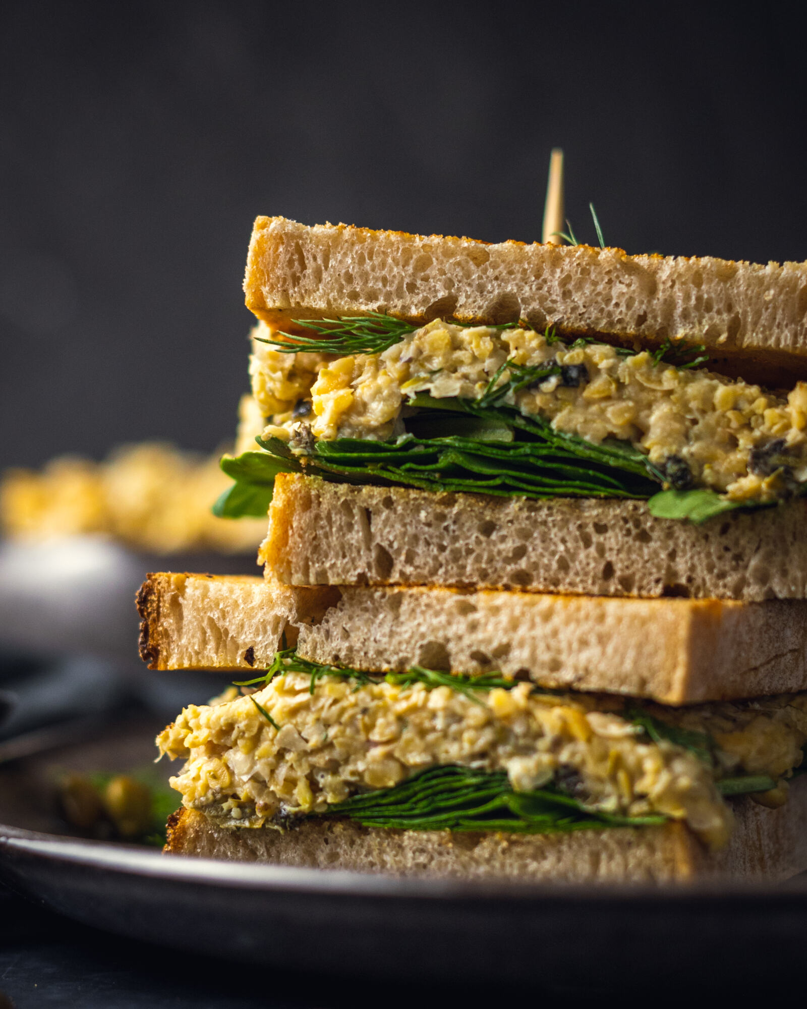 2 chickpea tuna sandwiches on top of each other on a black plate, shown up close