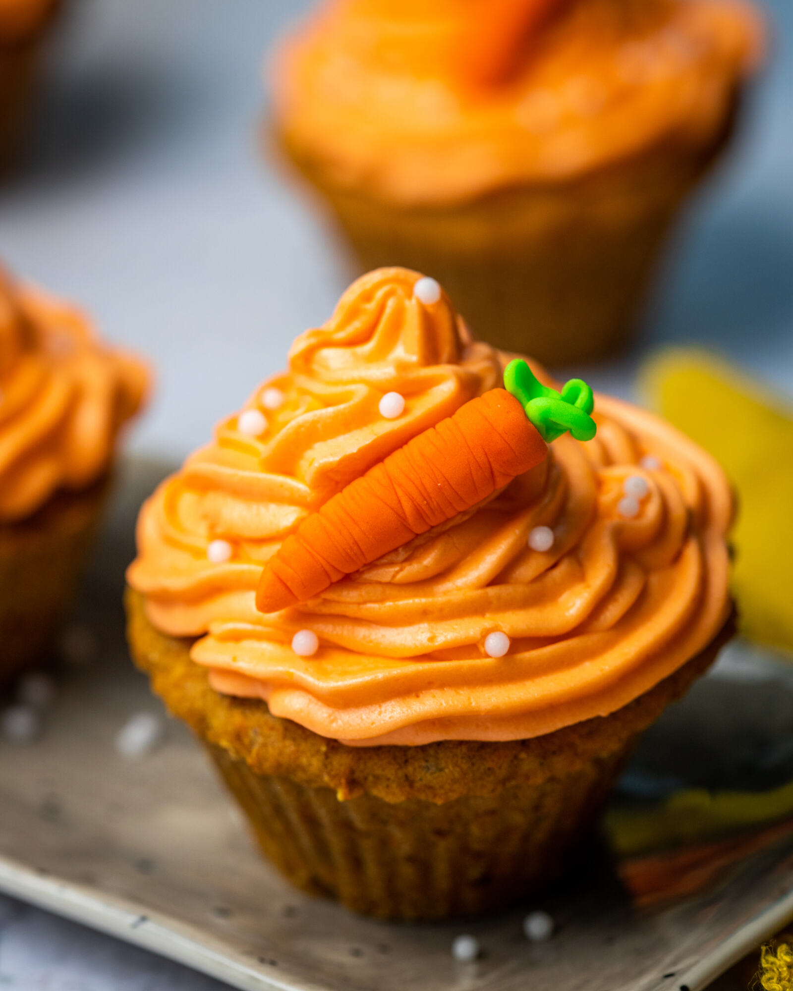 Close-up of the decoration on a carrot cake muffin with an orange buttercream and a tiny sugar carrot