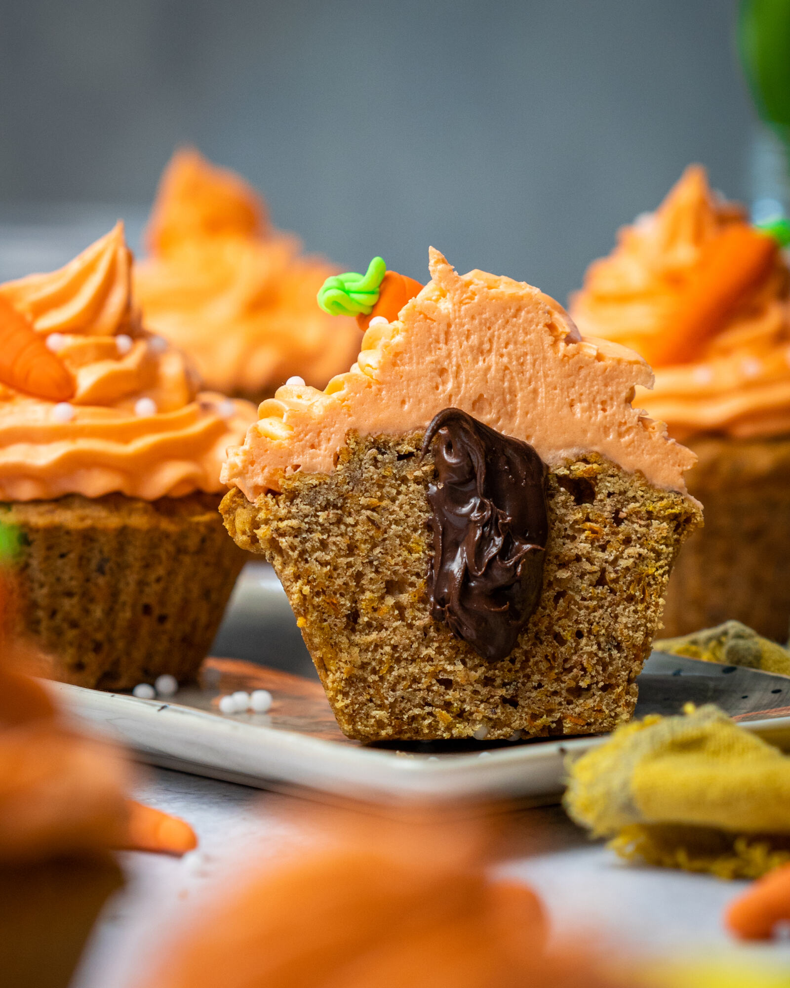 Vegan carrot cake muffins on a white tray, one in focus cut in half with chocolate coming out of it