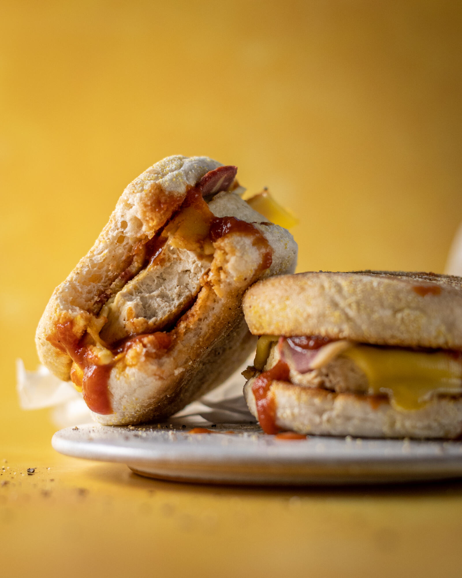 2 vegan egg mcmuffins on a white plate, one of them leaning on the other with a bite taken out of it, on yellow background