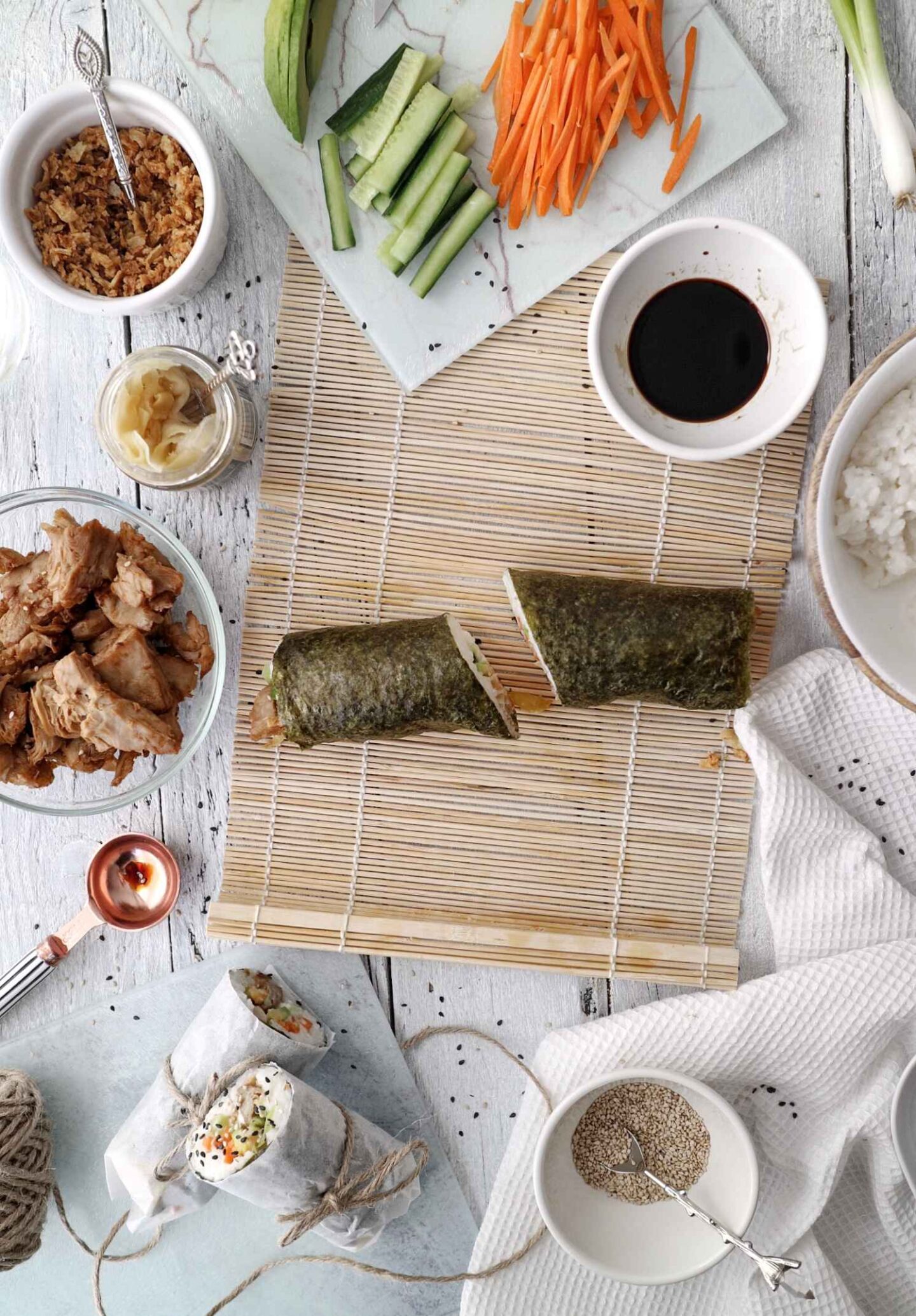 a vegan sushi burrito sliced into halves on a sushi mat with ingredients surrounding