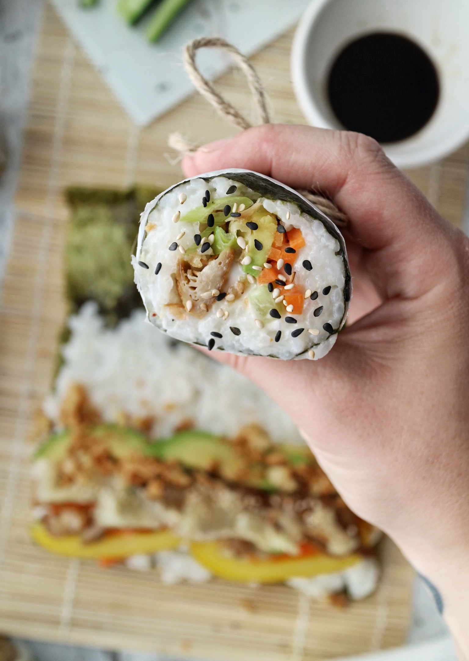 a hand holding a sushi burrito into the camera