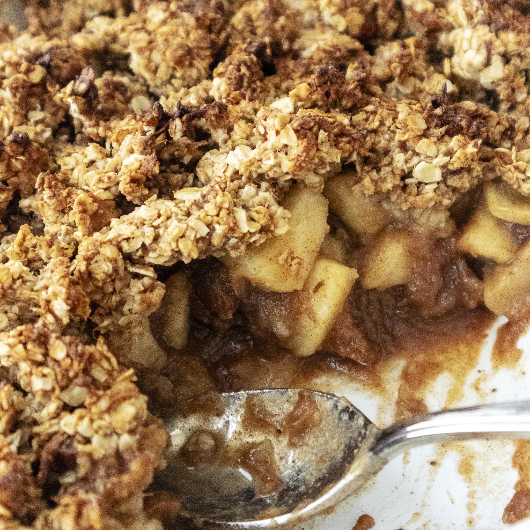 close of of a vegan breakfast crumble with apples and a spoon in the dish