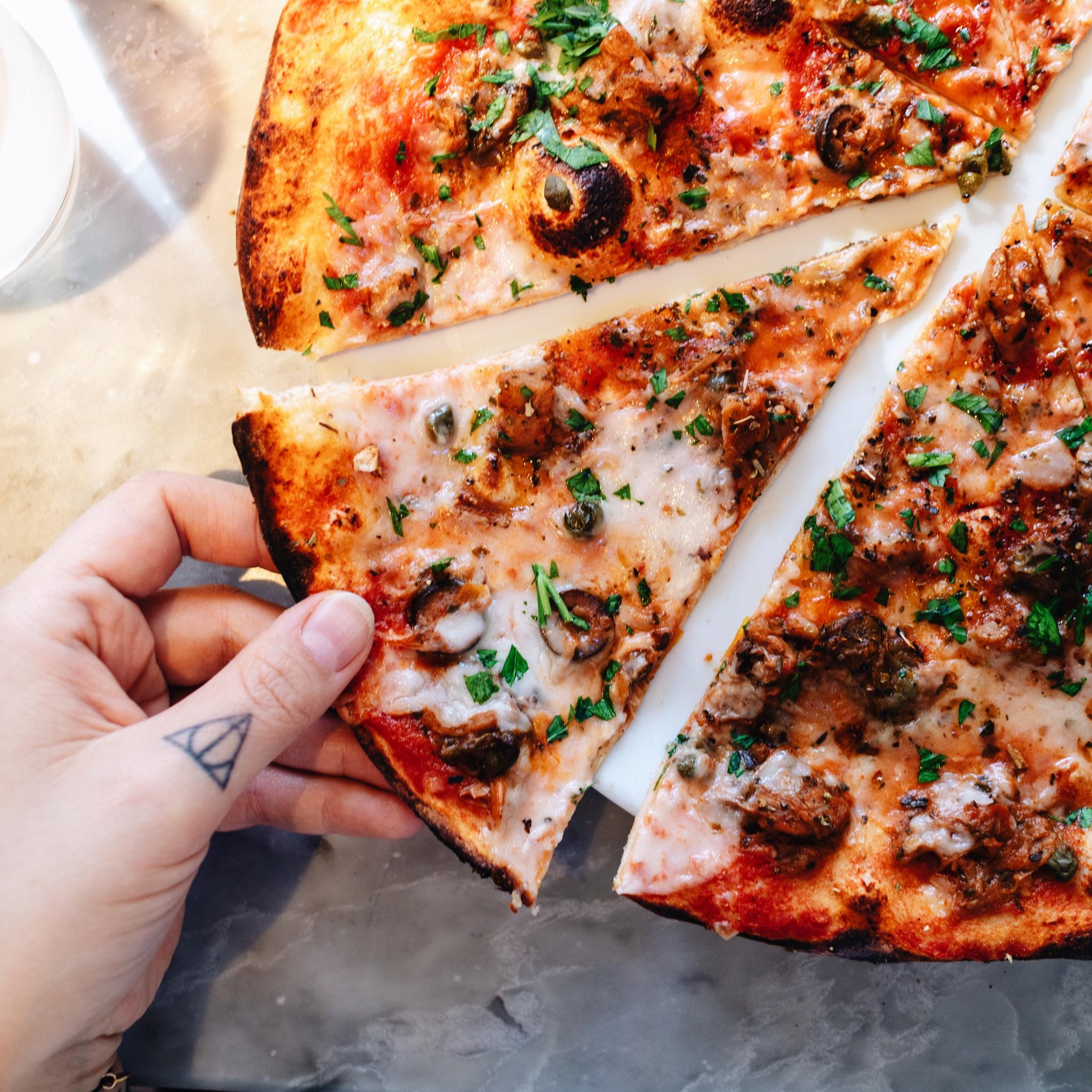 a hand picking up a slice of vegan pizza