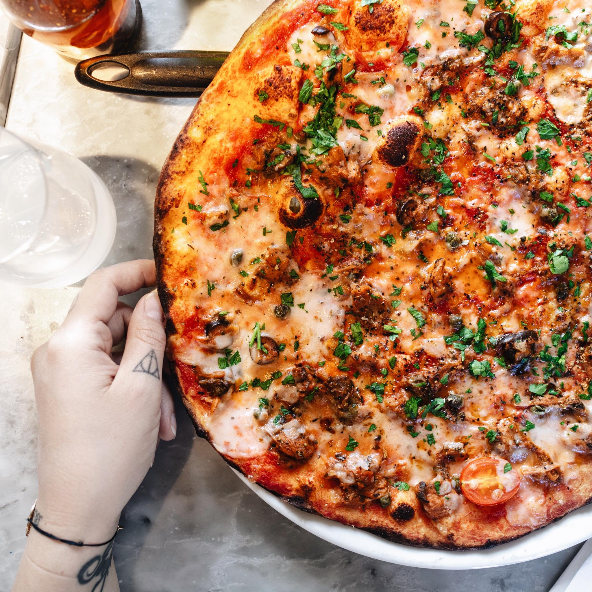 a hand next to a vegan pizza at pizza express