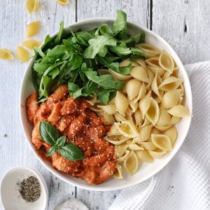 creamy roasted red pepper pasta in a bowl with rocket salad