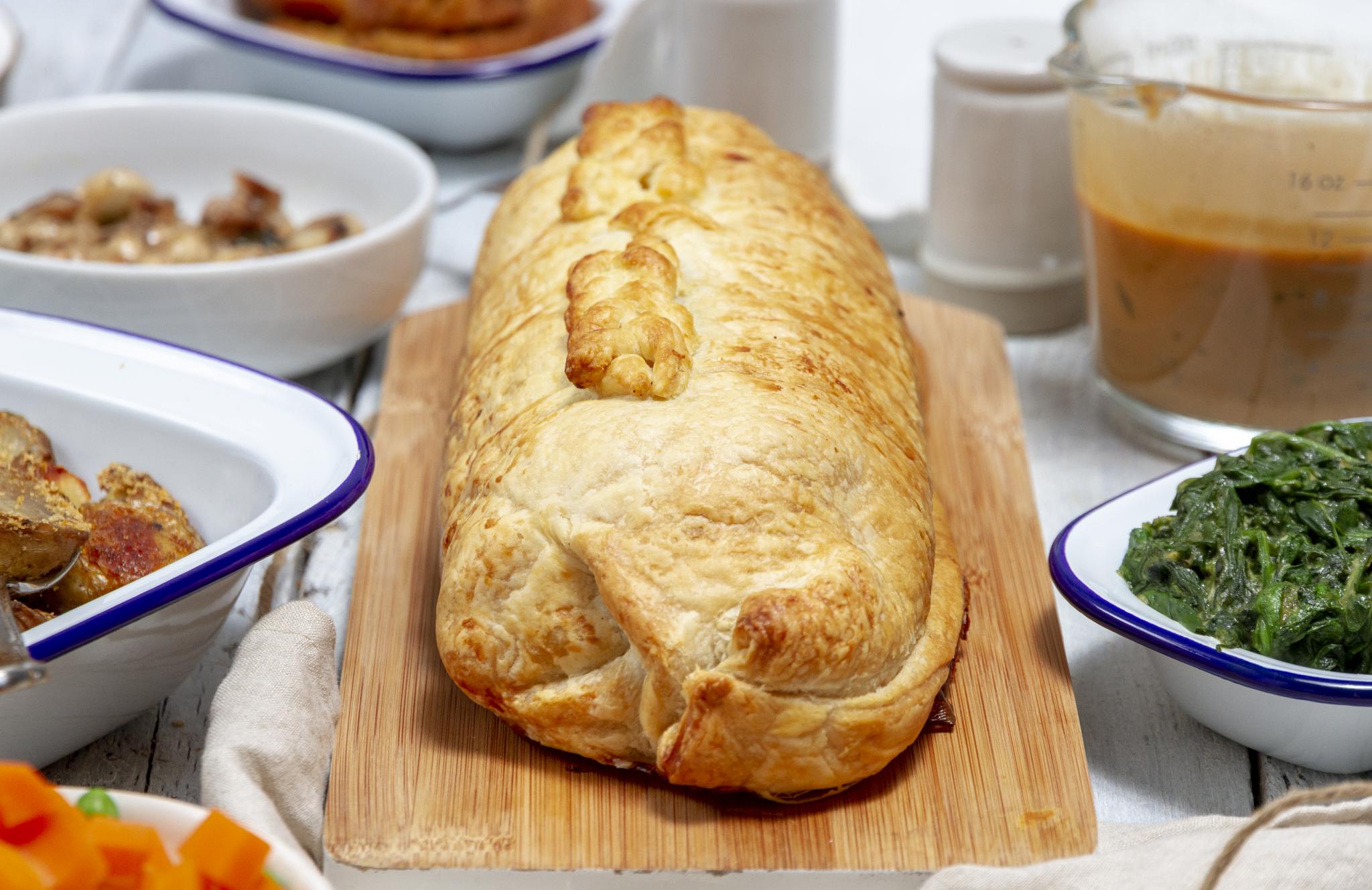 Festive Vegan Seitan Wellington, placed on a white table, surrounded by festive side dishes and a gravy jug