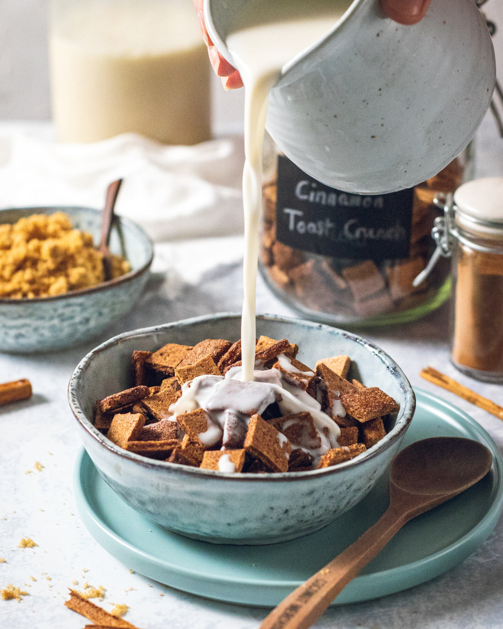 a jug of non-dairy milk being poured onto a bowl of vegan cinnamon toast crunch