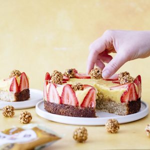 Mango Coconut Cake decorated with strawberries and Perkier bites and a hand placing more perkier bites on top