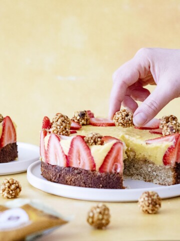 Mango Coconut Cake decorated with strawberries and Perkier bites and a hand placing more perkier bites on top