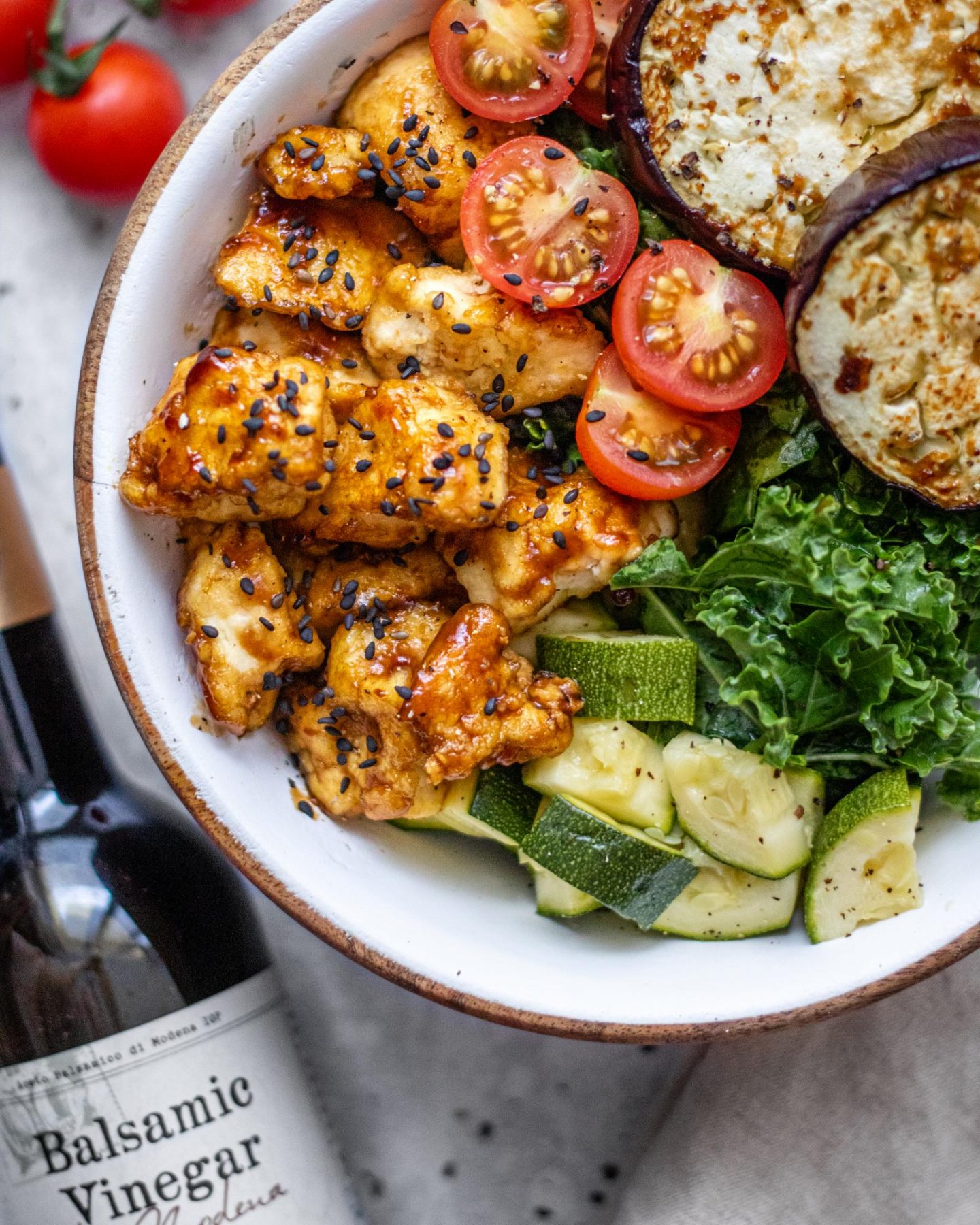 Sticky Balsamic Tofu is shown on top of a bowl of fresh and roasted vegetables.