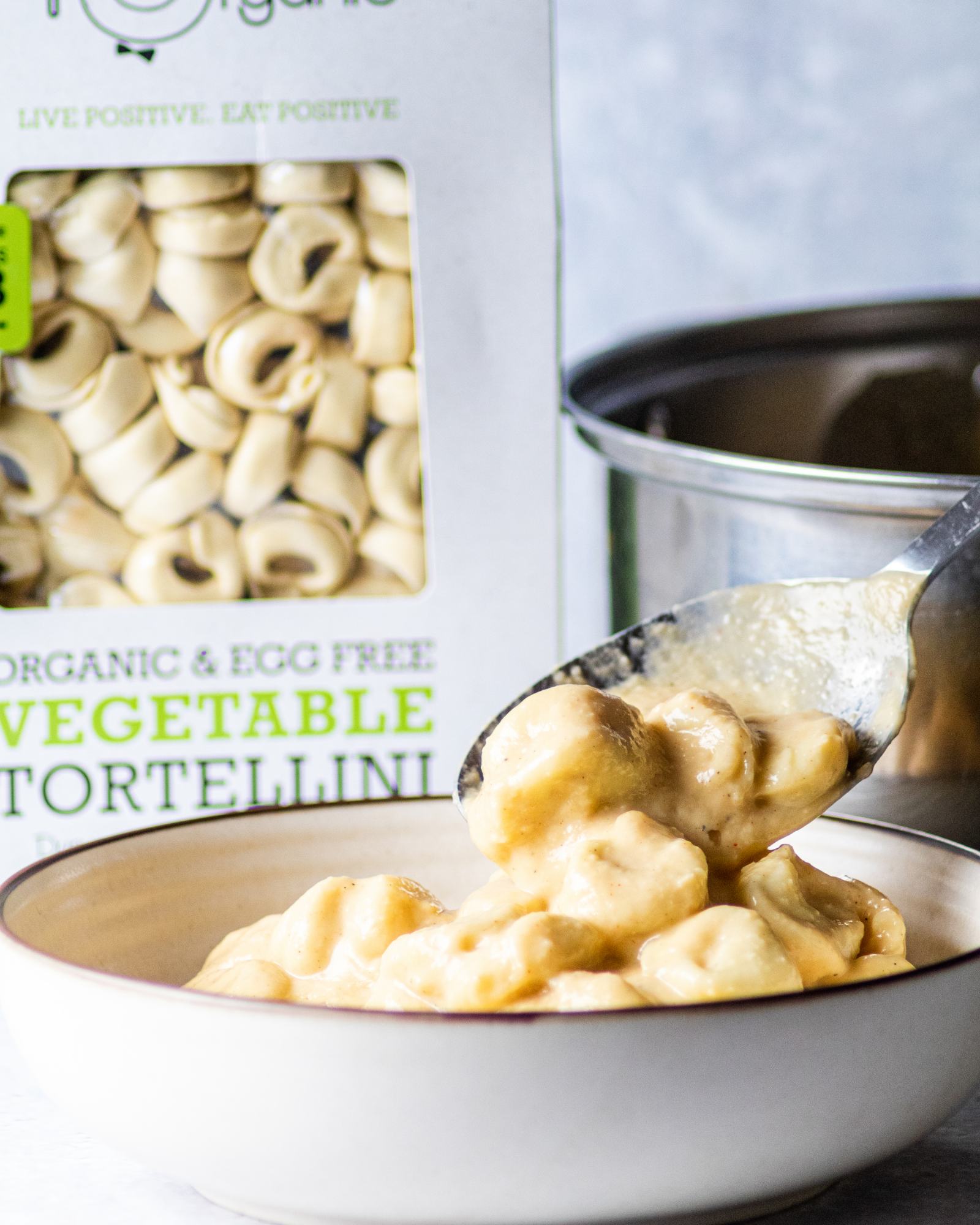 a large serving spoon placing creamy cauliflower alfredo tortellini into a serving plate.