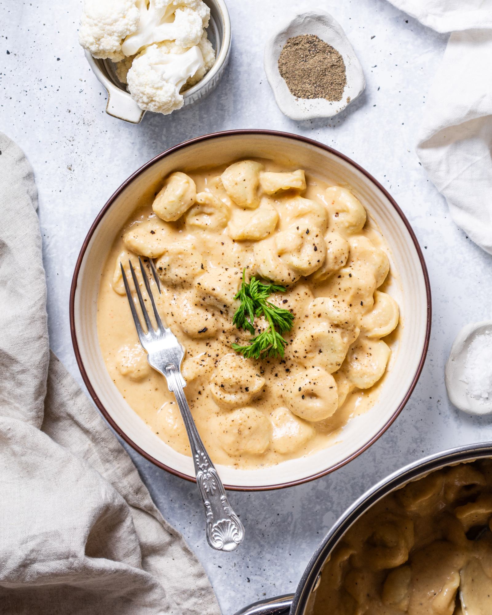 creamy vegan alfredo pasta in a white serving bowl with fresh herbs on top.