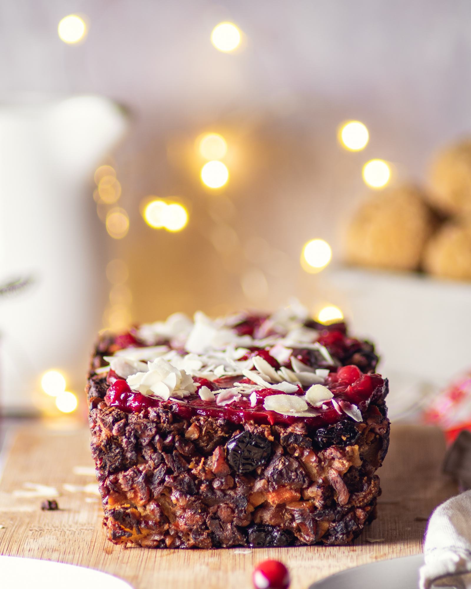 Easy Vegan Apple Nut Roast on a wooden board, topped with cranberry sauce and nuts, with fairy lights in the background