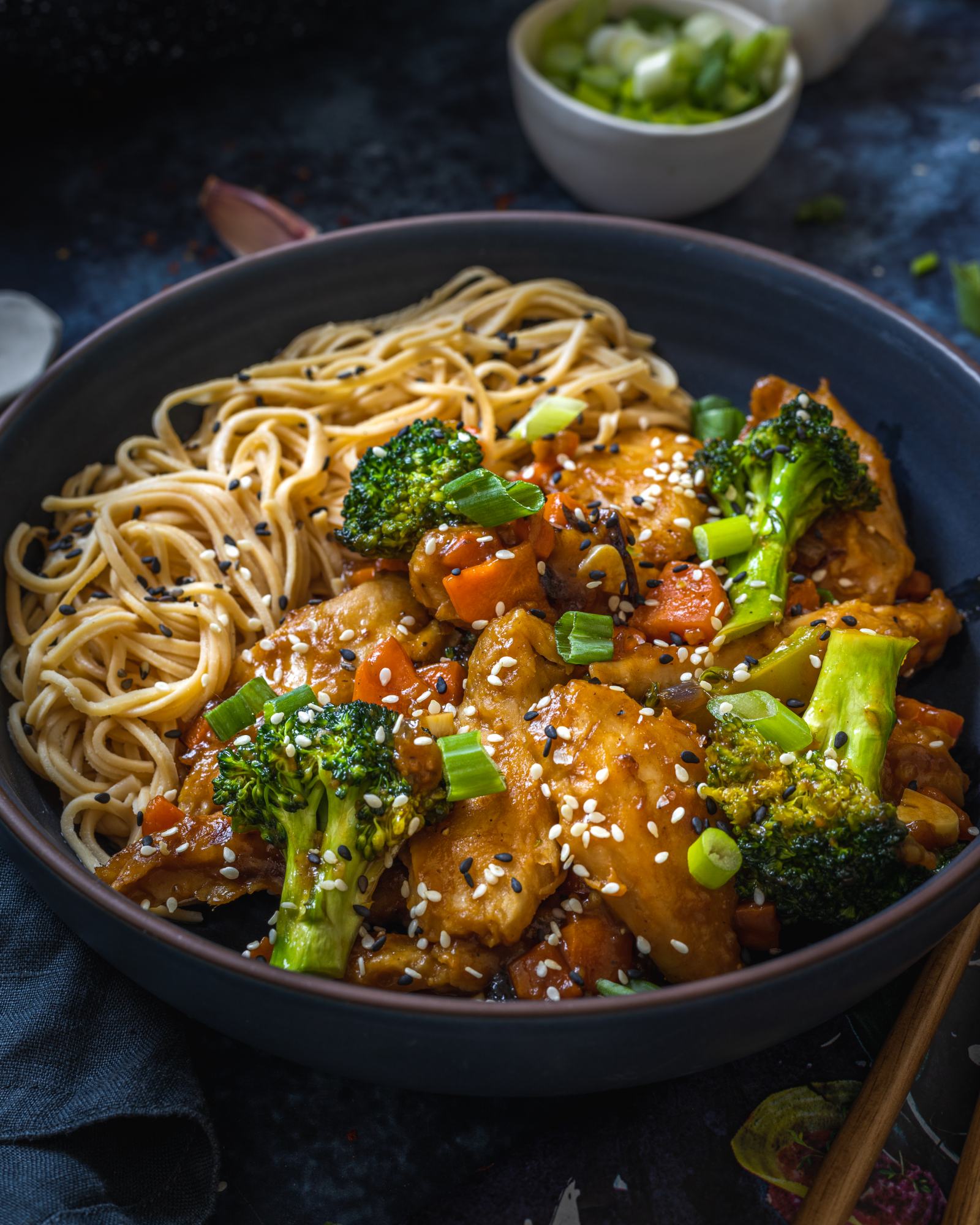 a black bowl filled with vegetables, noodles and teriyaki sauce