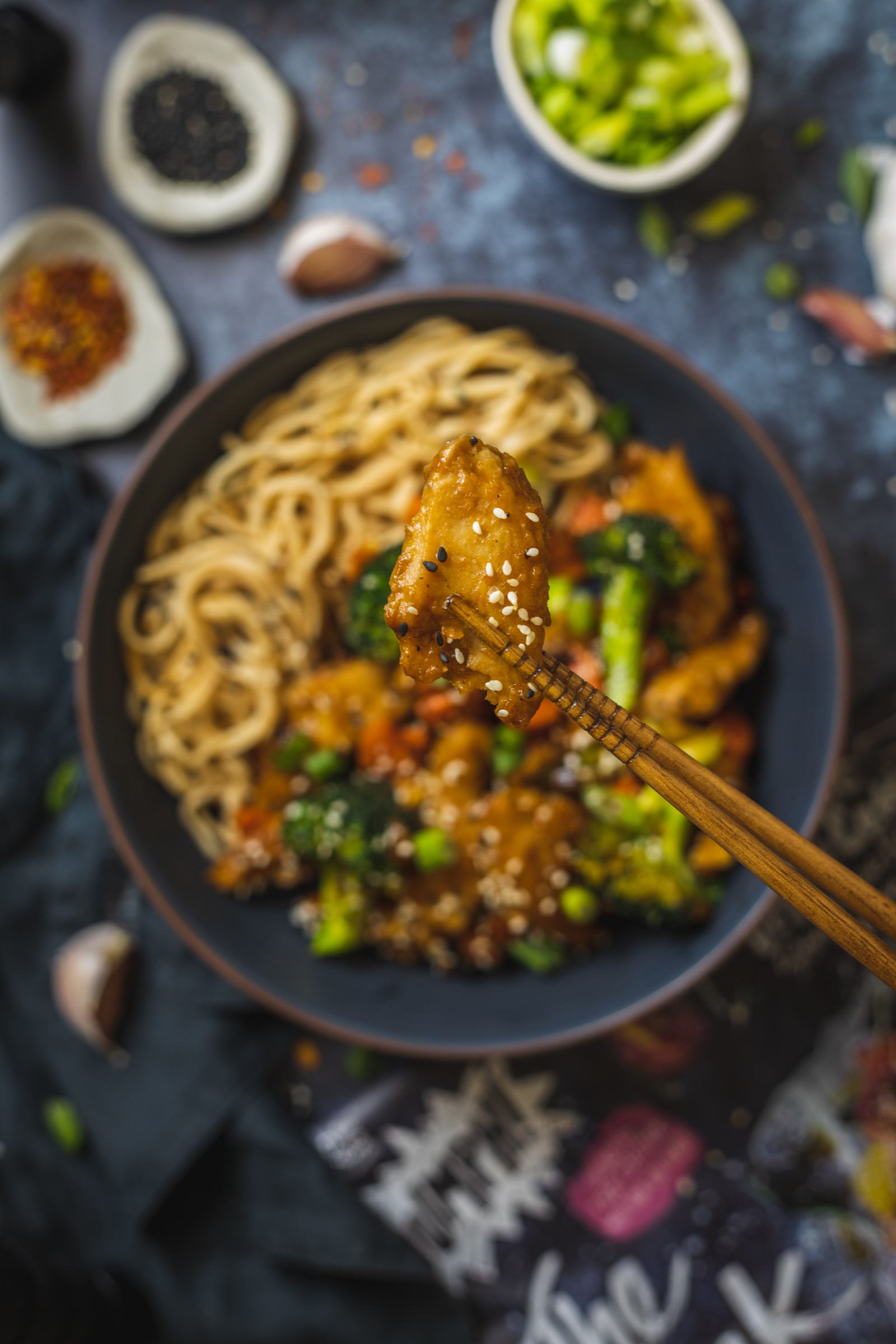 2 chopsticks holding a vegan chicken piece coated in vegan teriyaki sauce into the camera