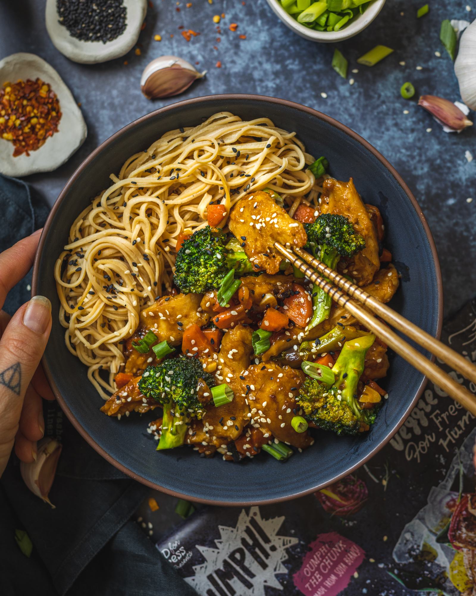 2 chopsticks holding a vegan chicken piece coated in vegan teriyaki sauce into the camera