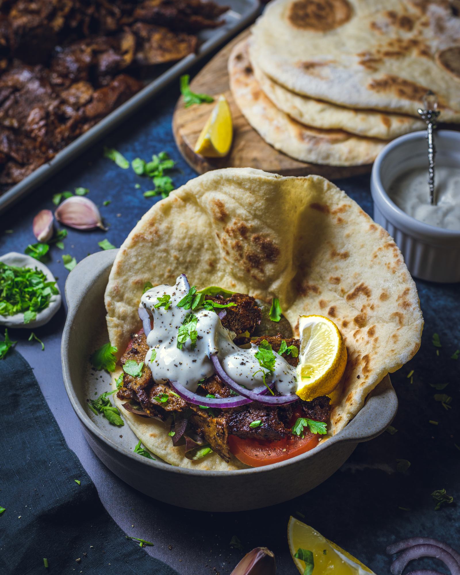 Vegan seitan kebab filling is sitting on an open pitta bread alongside sliced onions, tomatoes, salad and a slice of lemon.