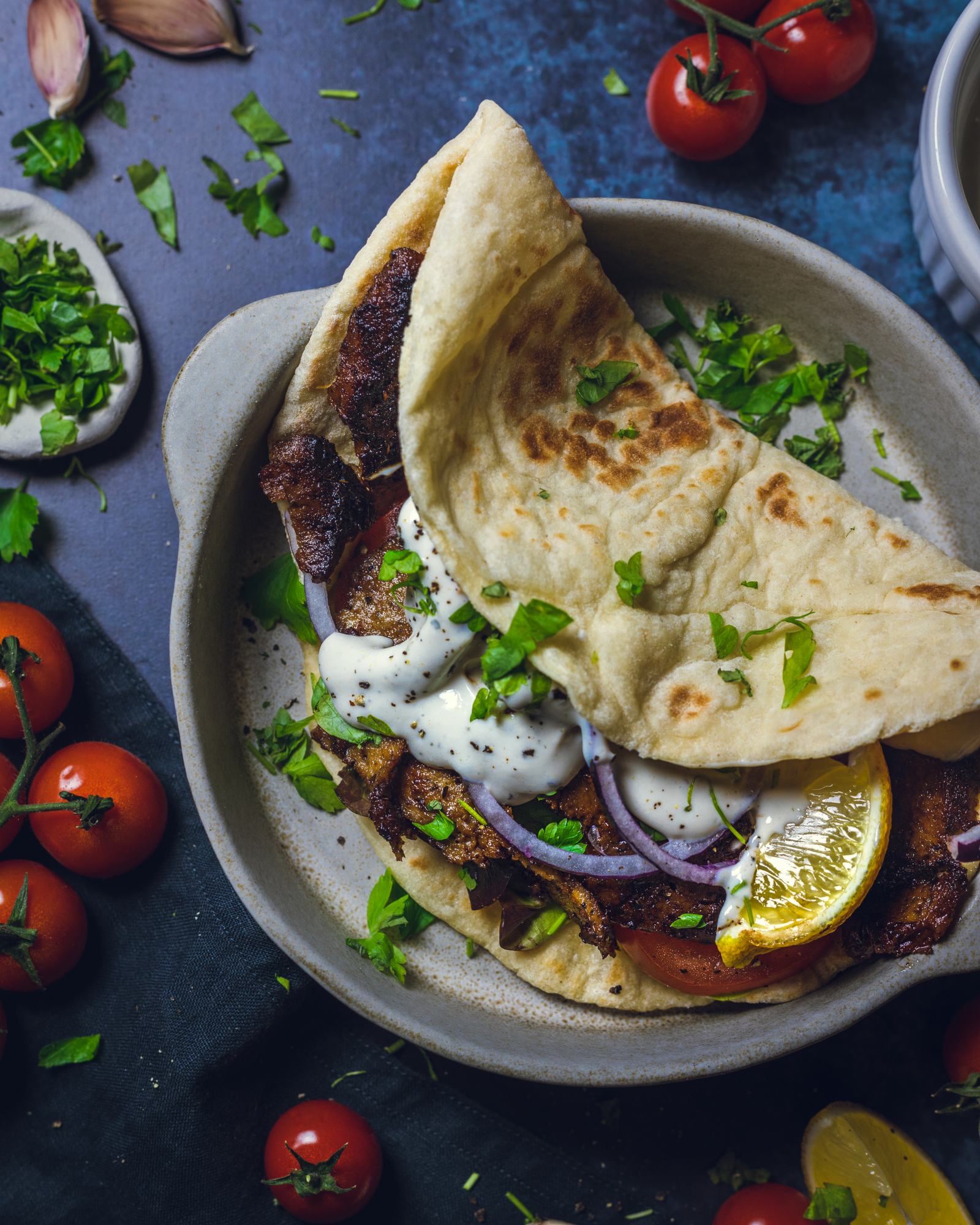 A Vegan Doner Kebab made of vegan seitan meat, tomatoes, herbs and red onion in a toasted pitta is served on a plate. 