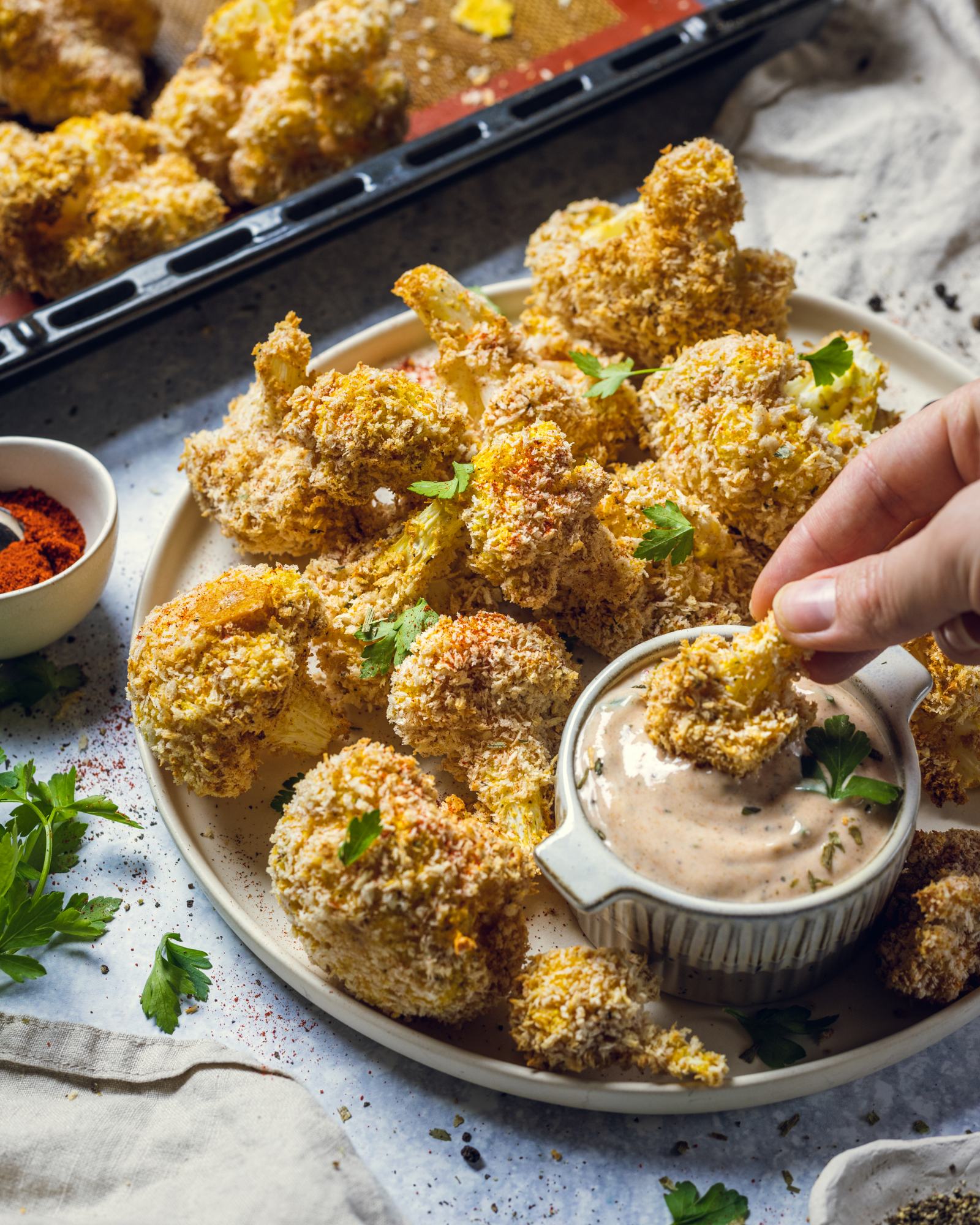 A hand is dipping a crispy cauliflower bite into a dip on a serving platter.