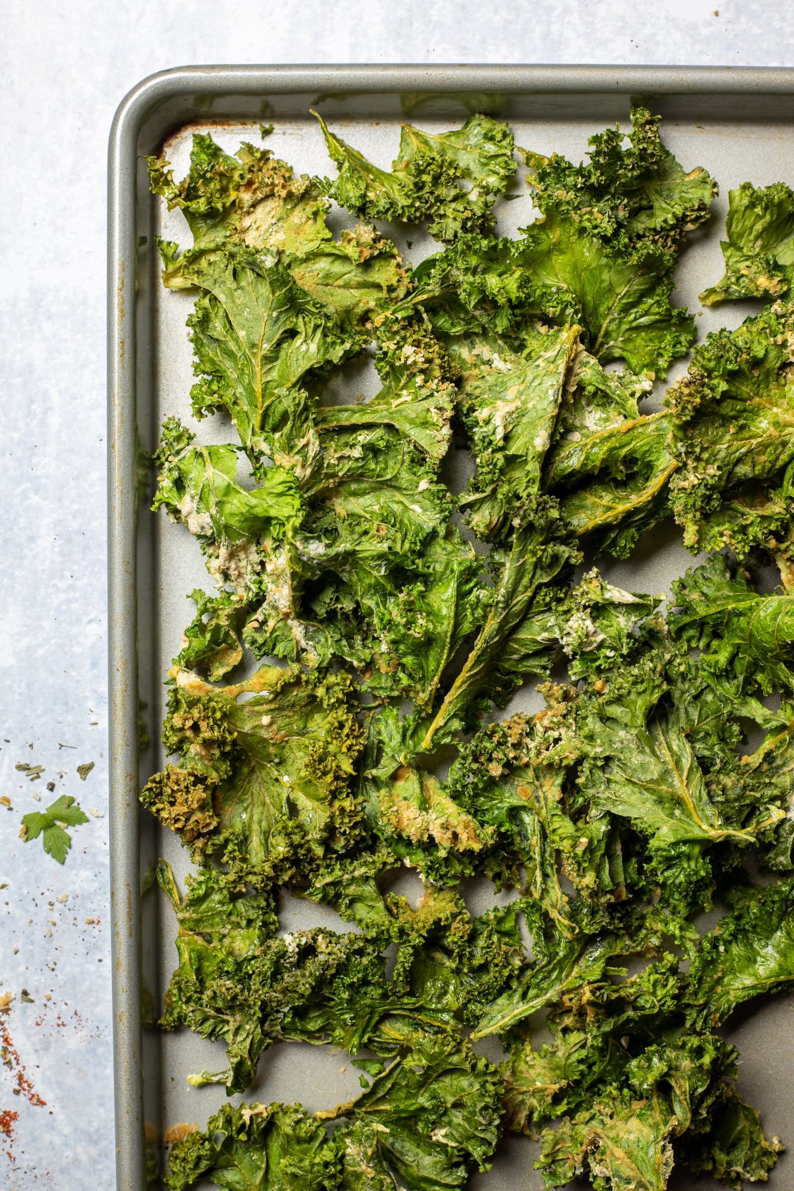 Crunchy kale chips are presented on a grey oven tray on a white table.