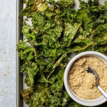 Air fryer kale chips on a tray with a bowl of vegan cheese and onion seasoning next to it