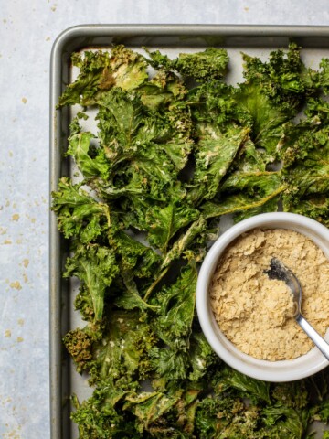 Air fryer kale chips on a tray with a bowl of vegan cheese and onion seasoning next to it