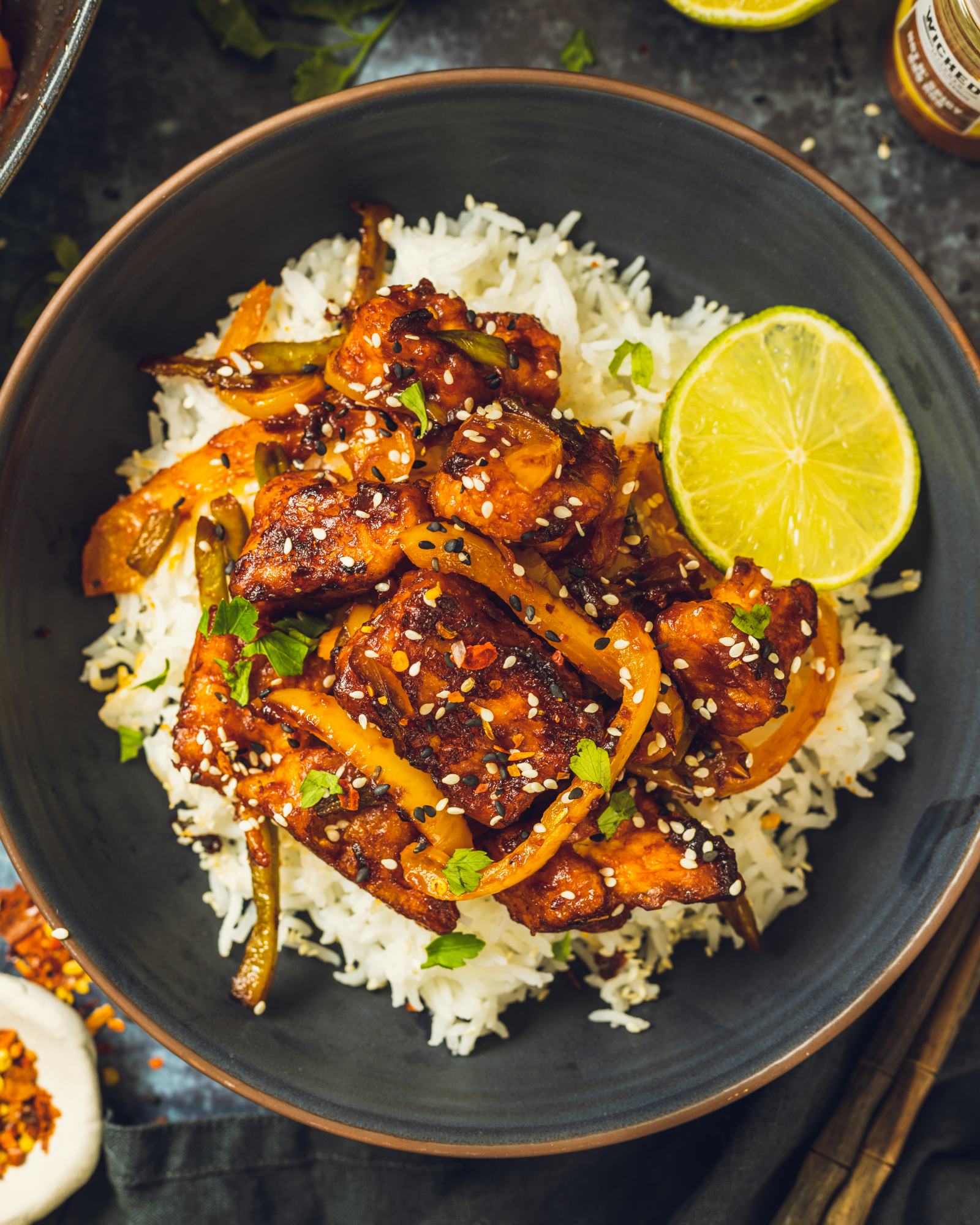 A bowl of rice topped with sticky BBQ tofu and vegetables on top is shown up close.