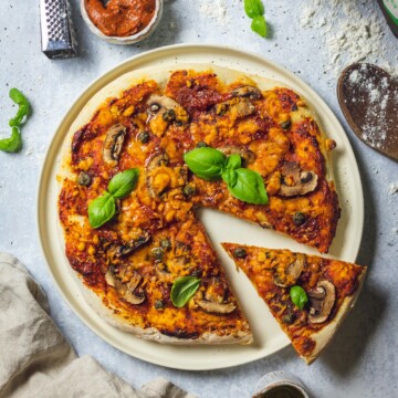 Homemade vegan pizza on a serving plate with one slice cut out of it