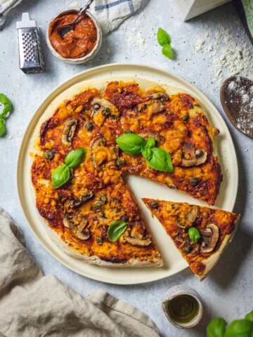 Homemade vegan pizza on a serving plate with one slice cut out of it