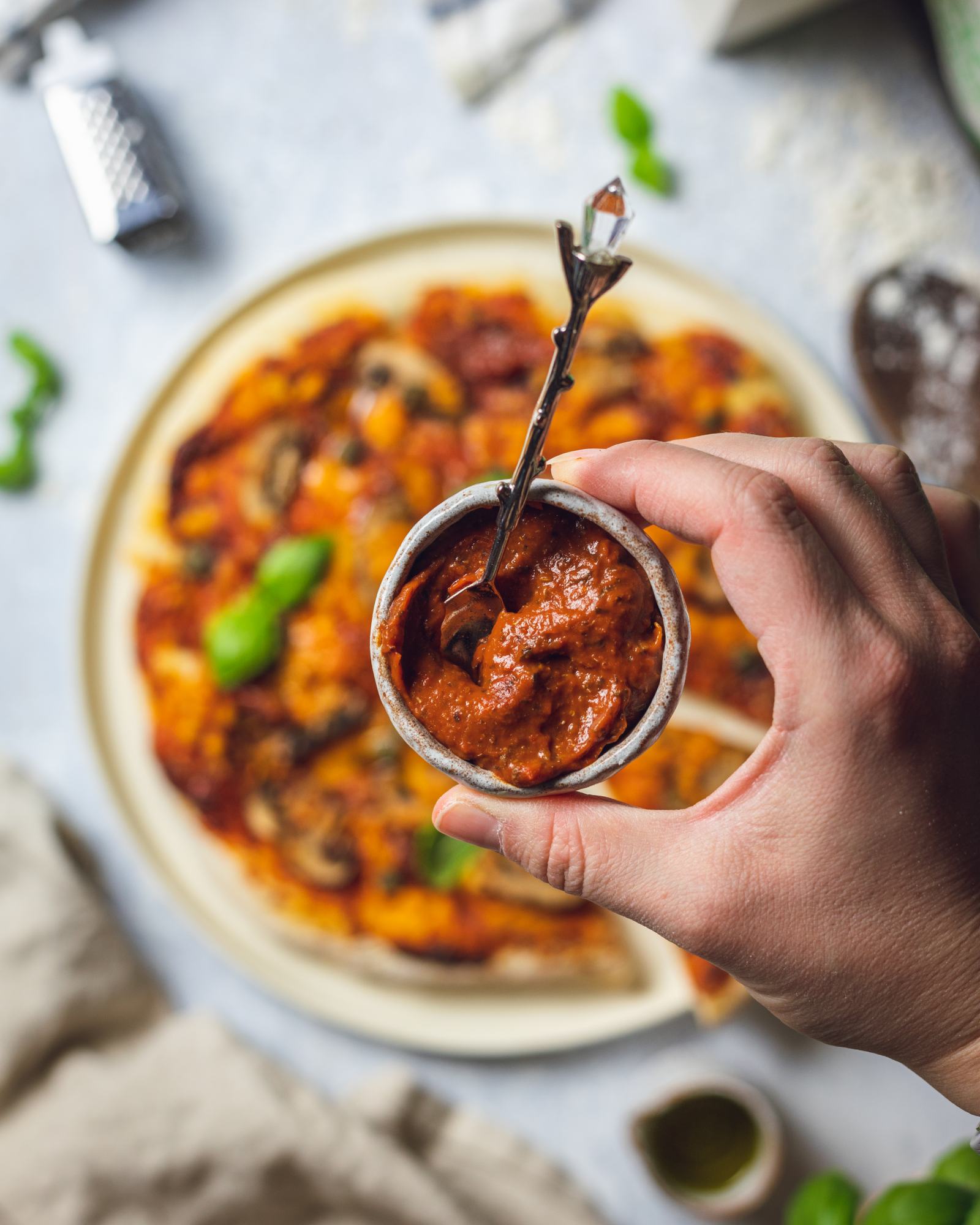 a small pot with homemade roasted tomato pizza sauce held by a hand over a pizza