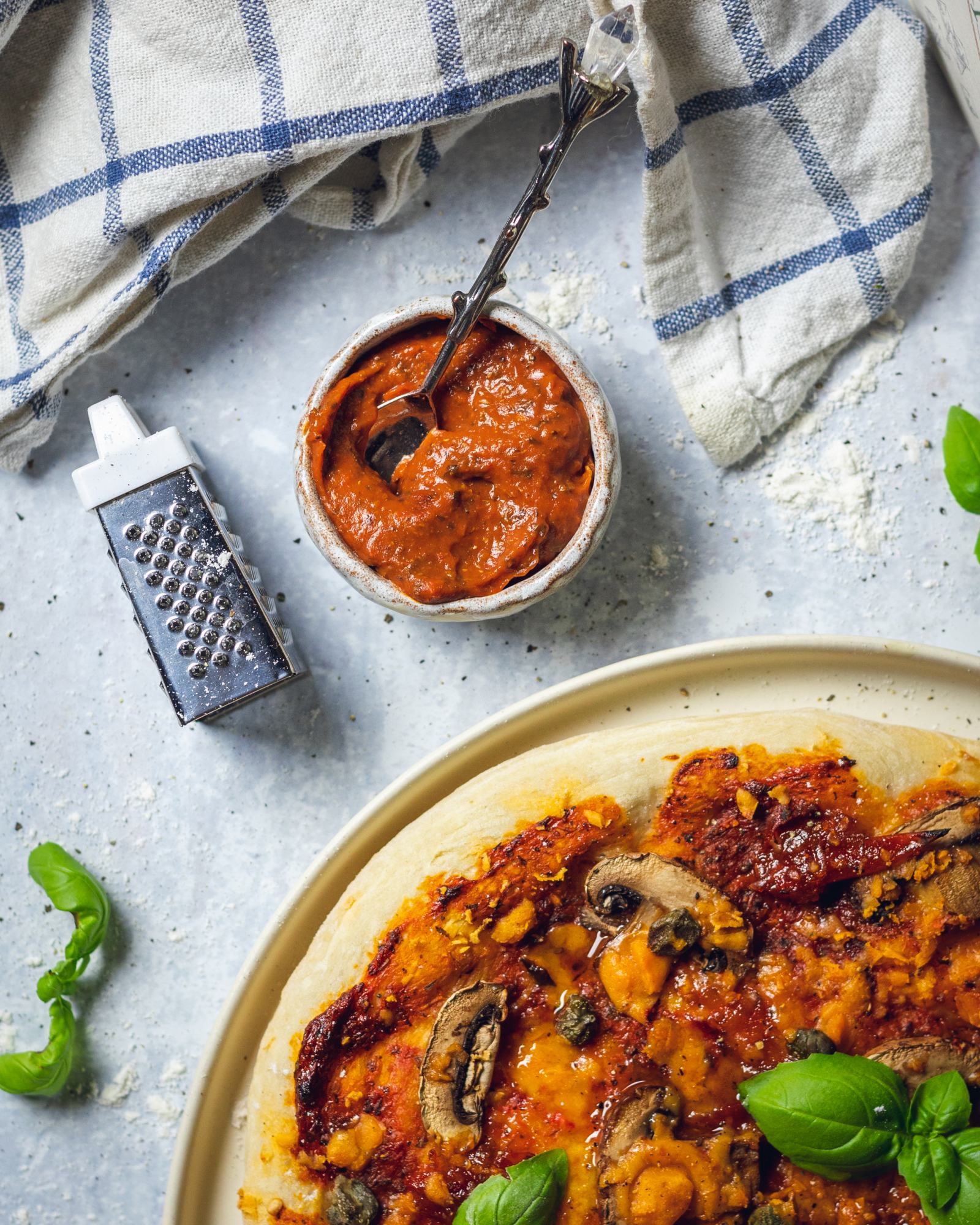 a small pot of homemade tomato sauce for pizza on a while table next to a pizza