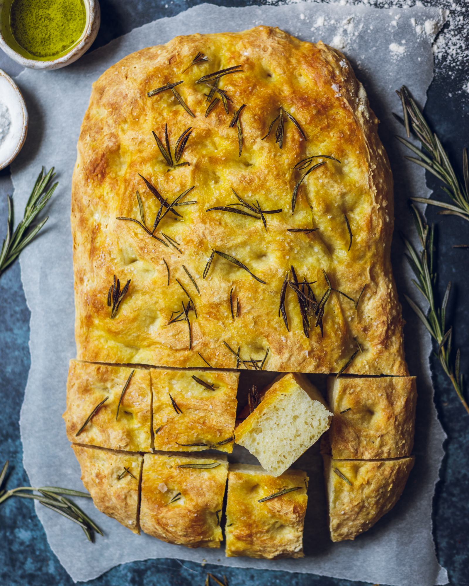 A whole loaf of vegan focaccia with half sliced into portion-size cubes. One of the cubes is flipped sideways, so you can see the fluffy texture of the bread.