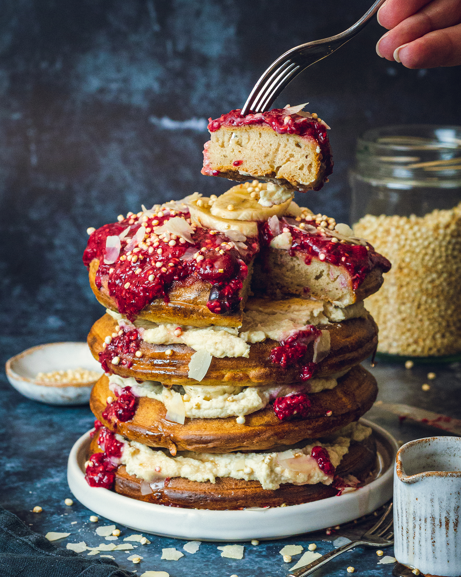 a fork lifting a piece of a vegan American-style pancake with chia jam on top out of a pancake stack.