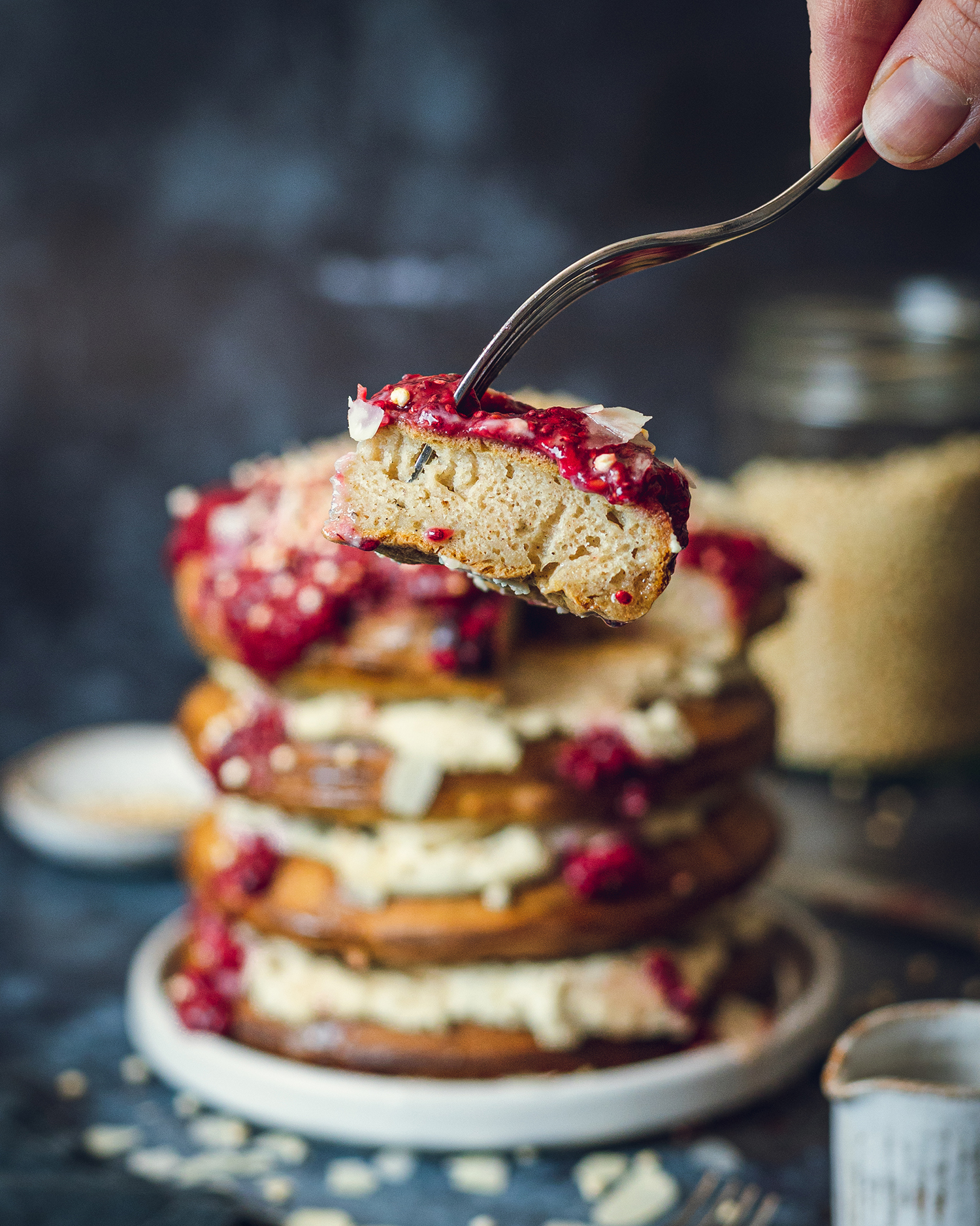 a fork holding a piece of a vegan American-style pancake with a stack of 4 soft and fluffy vegan pancakes in the background