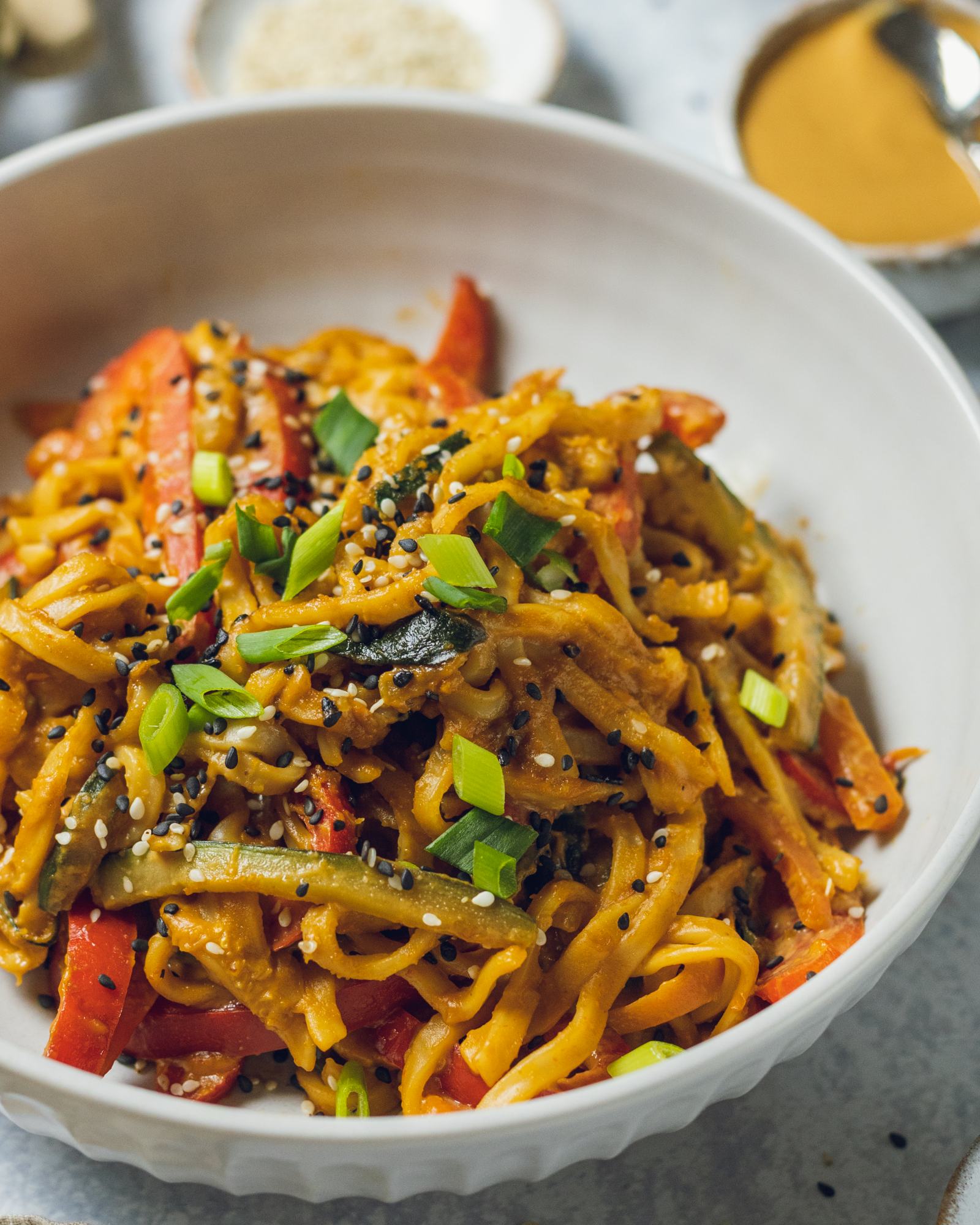 A bowl of vegan peanut noodles is shown up close with the creamy thai peanut sauce visible on the thick noodles.