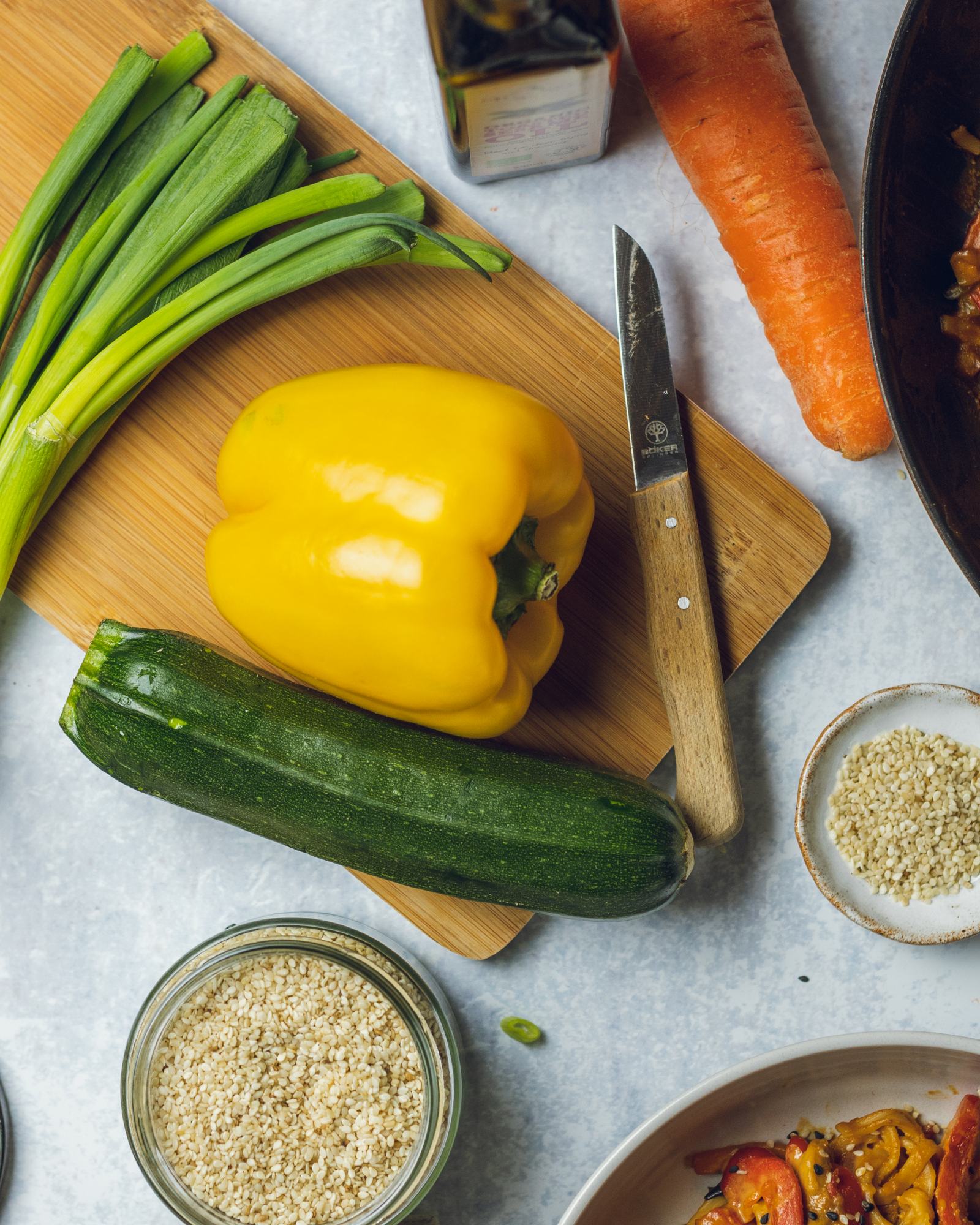 Fresh vegetables for the peanut noodles recipe are shown on a cutting board such as green onions (spring onions), bell pepper, zucchini and carrot.