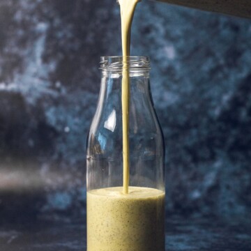 A hand pouring vegan caesar dressing from a blender into a glass bottle.