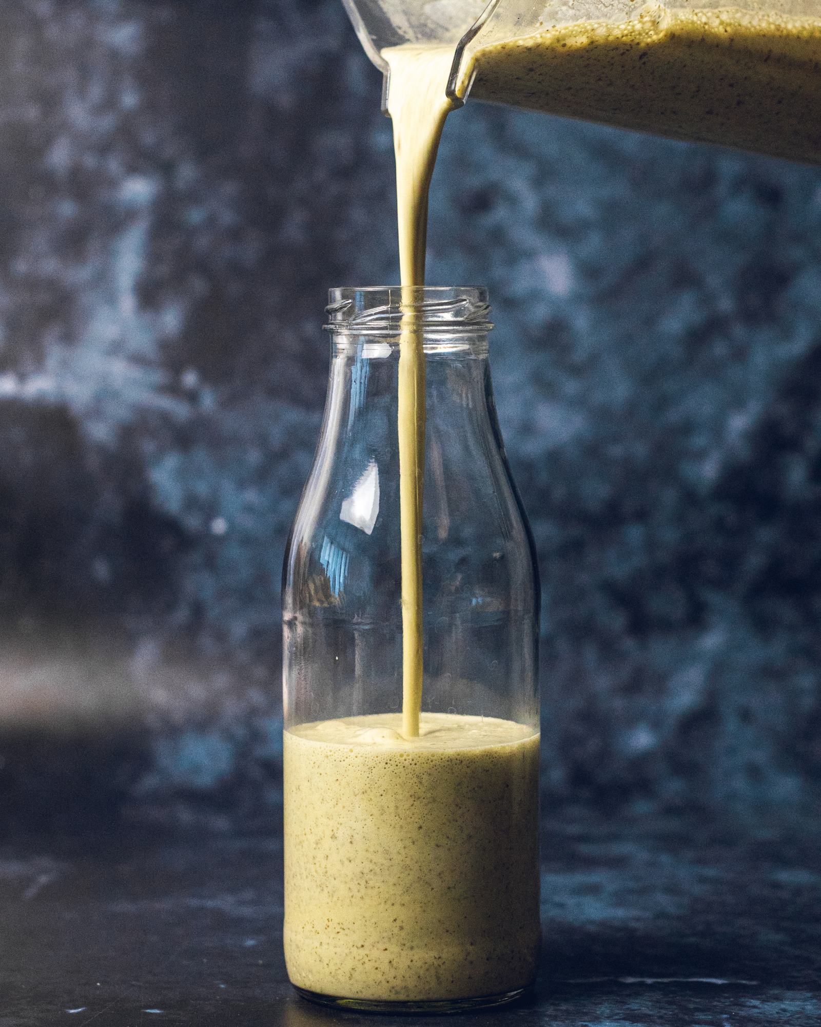 A hand pouring vegan caesar dressing from a blender into a glass bottle.