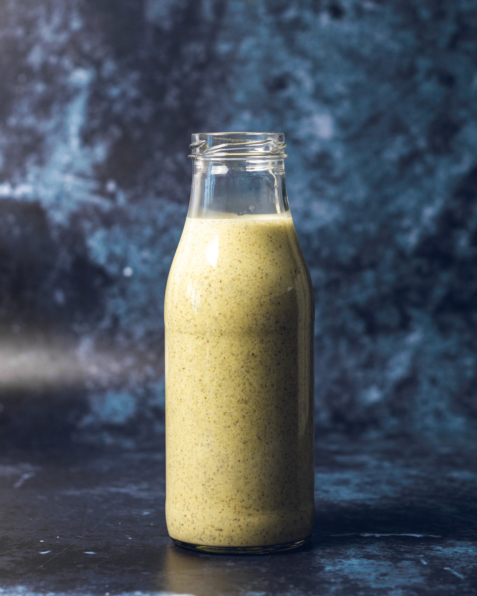 Vegan Caesar Salad Dressing in a large glass bottle is standing on a dark blue table in front of a blue wall.