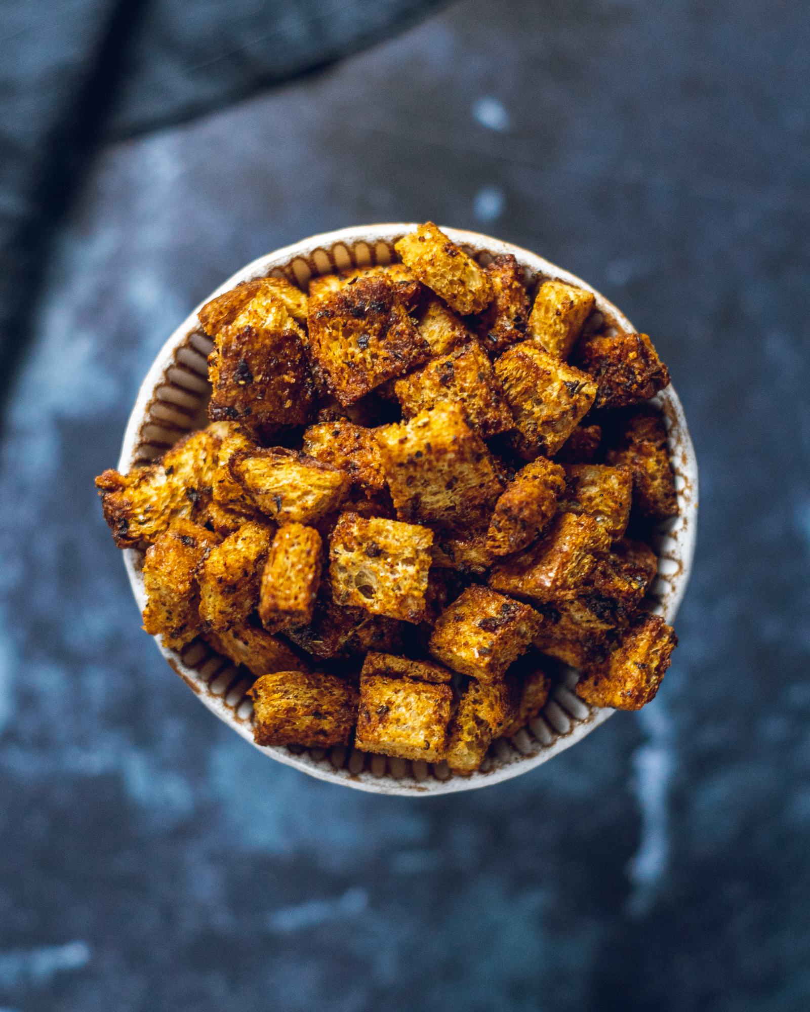 Garlic and Herb Croutons sitting in a small round bowl on a dark blue table.