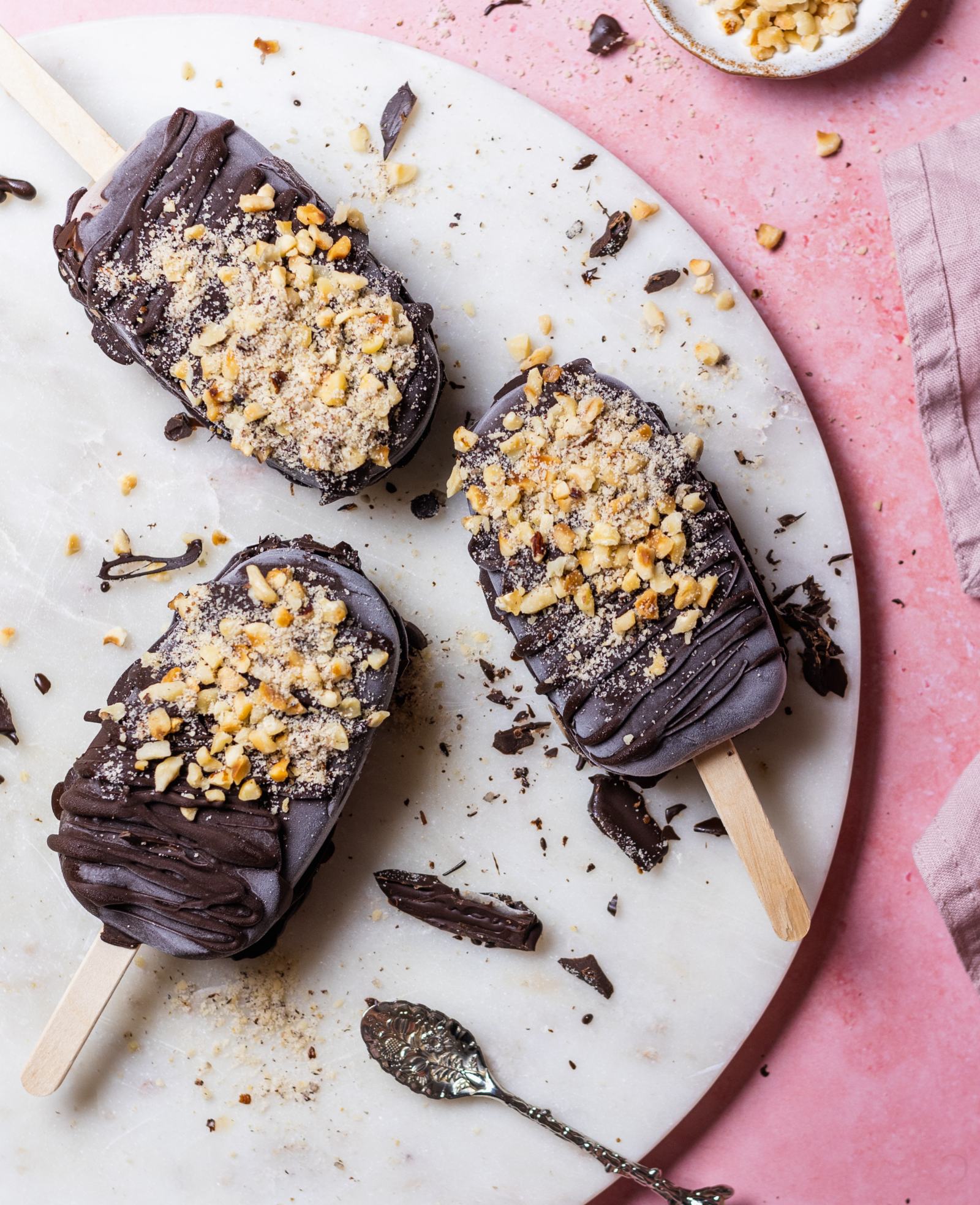 Vegan Chocolate Hazelnut Magnum Ice Cream, 3 laying on a white marble board with hazelnuts surrounding